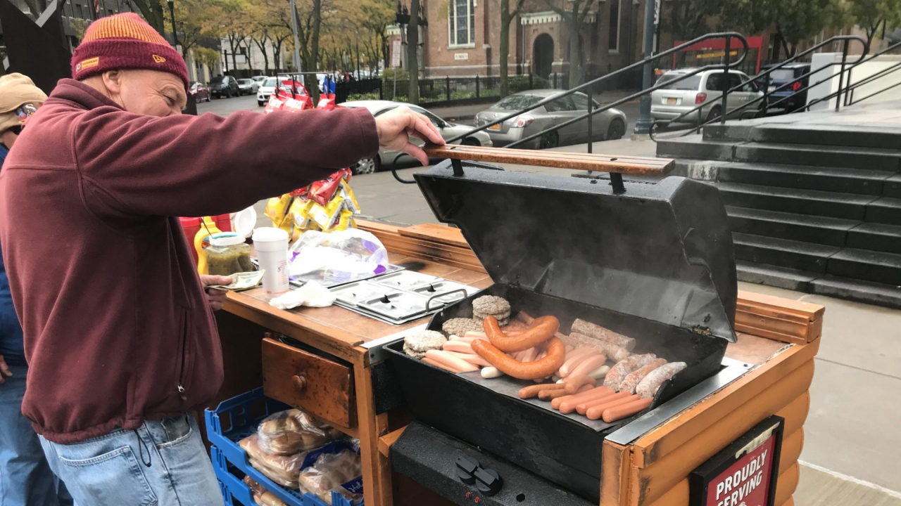 Paul Waleski starts grilling hot dogs, sausages, and hamburgers in preparation for hungry customers.